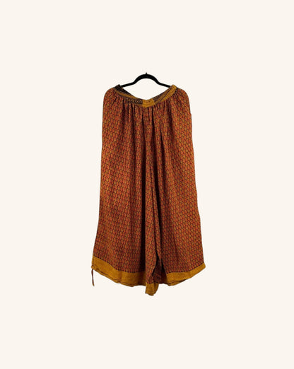 She Lives Beauty wide leg jogger pants in vintage orange and yellow patterned rasgulla silk on a hanger.