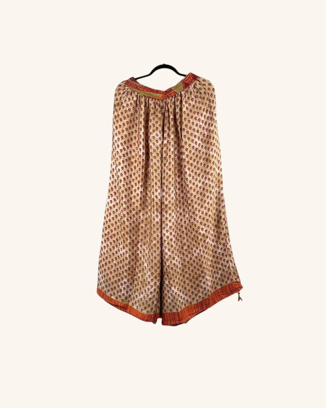She Lives Beauty vintage rasgulla silk wide leg pants in a beige and red patterned fabric on a hanger.